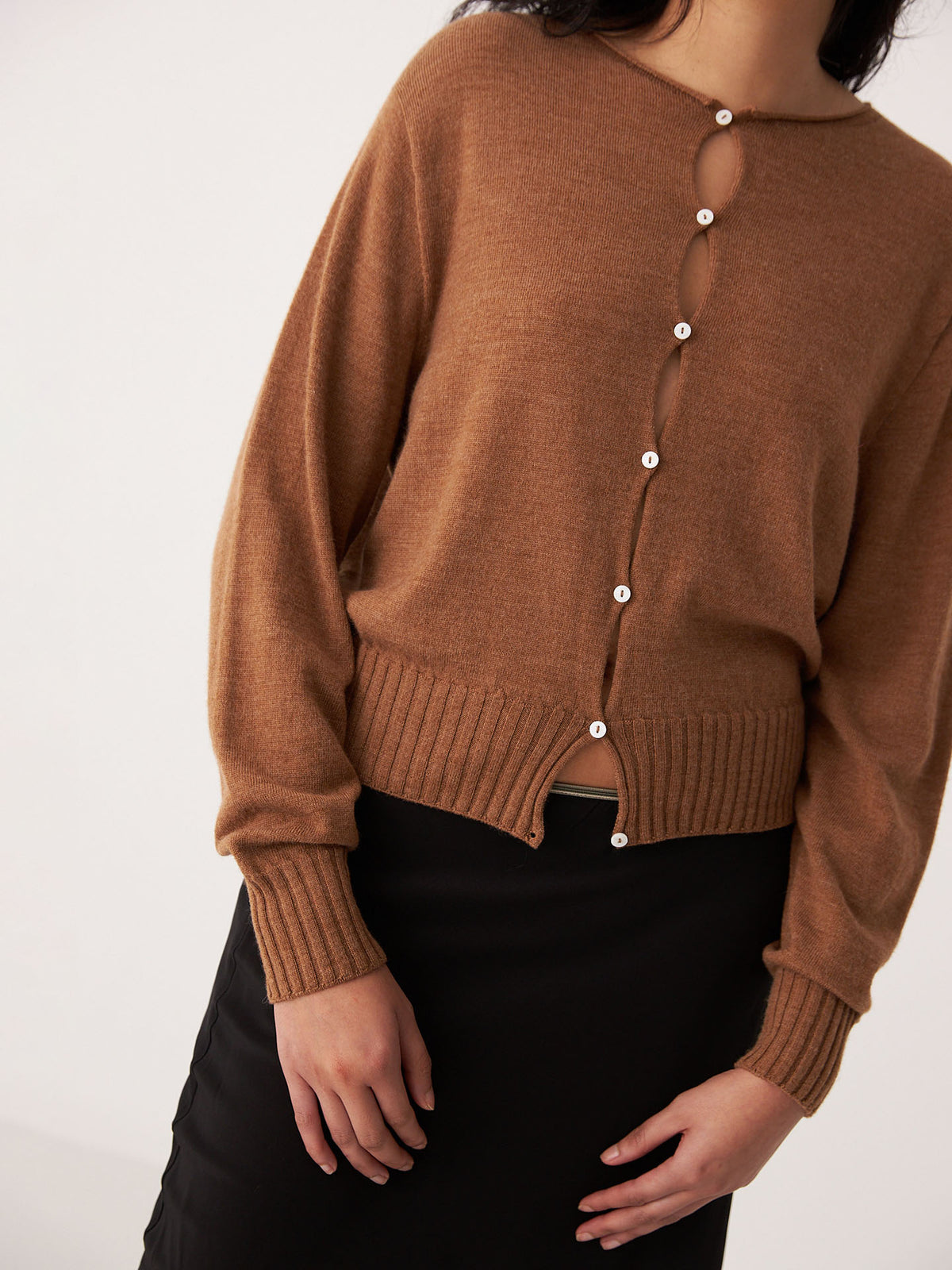 A person wearing the Francie Anni Cardigan in Brown Sugar with white buttons and a black skirt, standing against a plain light background.