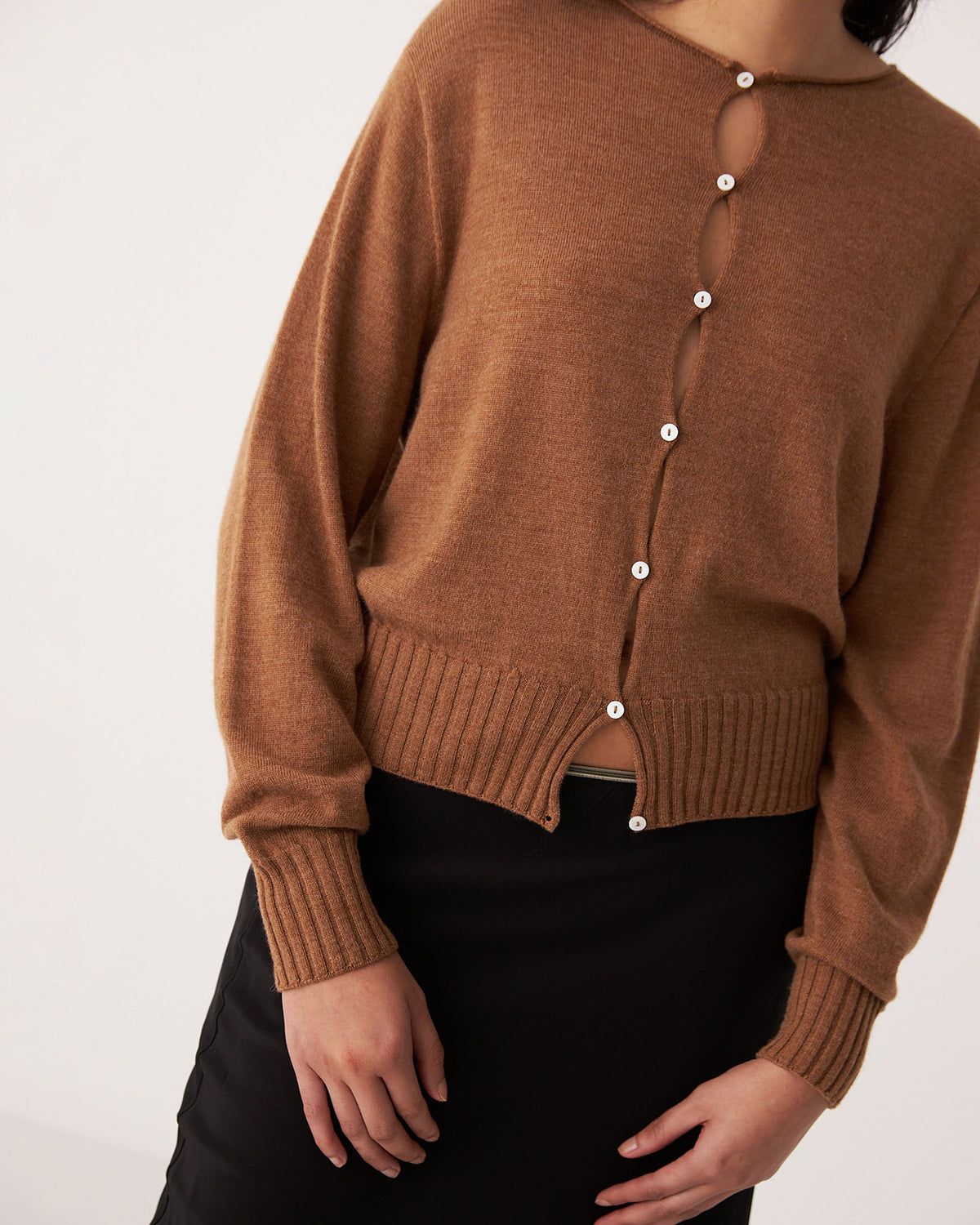 A person wearing the Francie Anni Cardigan in Brown Sugar with white buttons and a black skirt, standing against a plain light background.