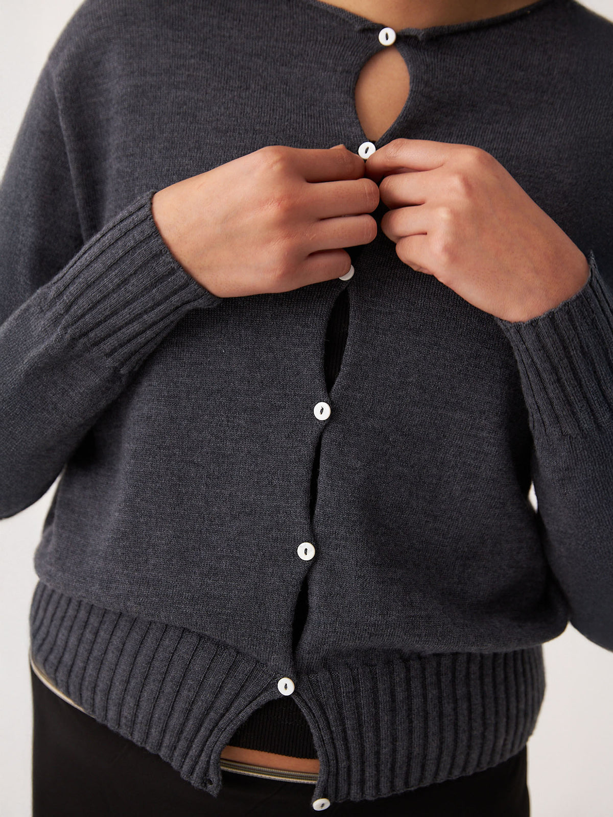 Someone buttons up the Francie Anni Cardigan in Shadow Grey, a relaxed-fit, dark gray knit with white buttons, shown from shoulders to hips.