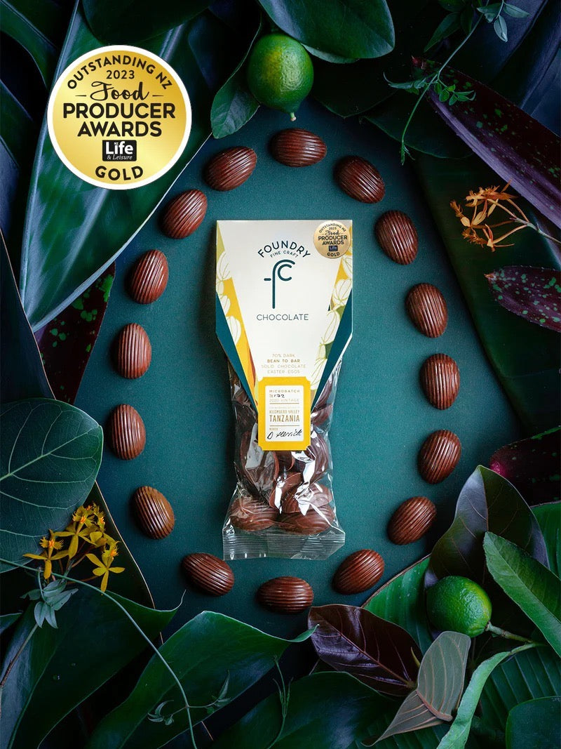 Award-winning Foundry Chocolate Tanzania 70% Mini Chocolate Eggs surrounded by fresh ingredients and leaves on a dark background.