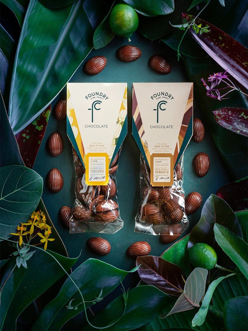 Two packages of Foundry Chocolate Mini Chocolate Eggs – Twin Pack amid a lush arrangement of green leaves and decorative elements.