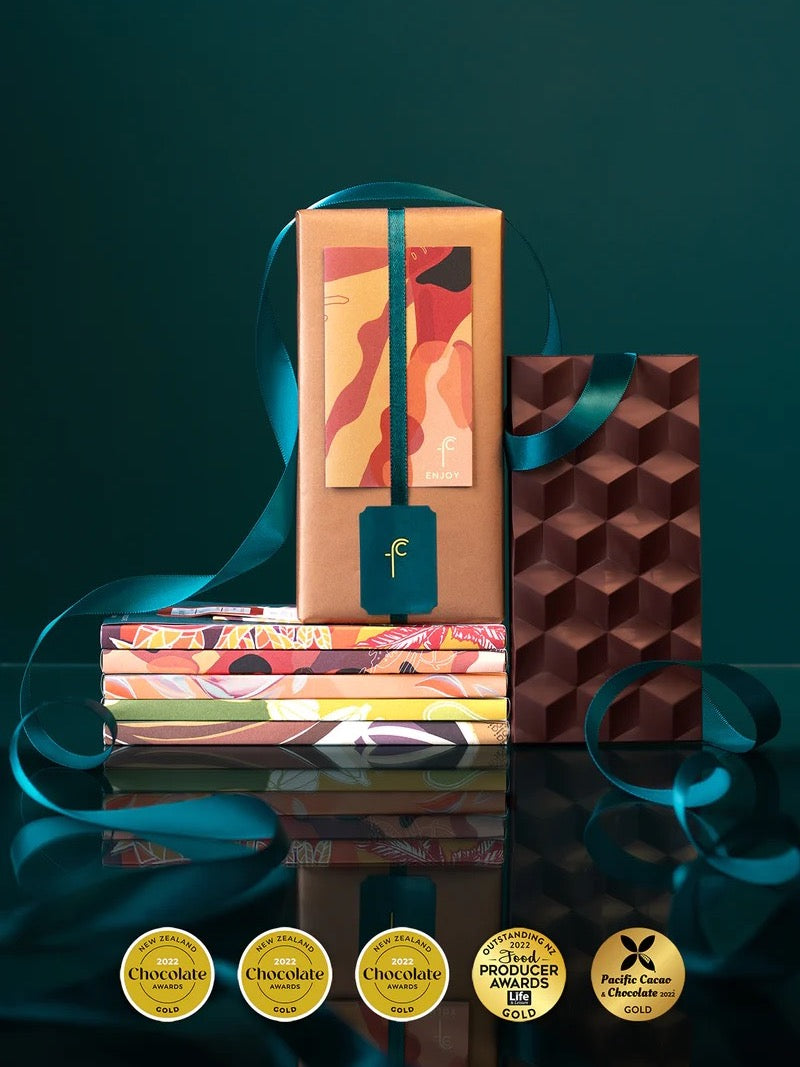 A box of Five Origin Gift Pack - Gold Winners chocolates from Foundry Chocolate with a ribbon on top, showcasing gold winning flavors and enticing tasting notes.