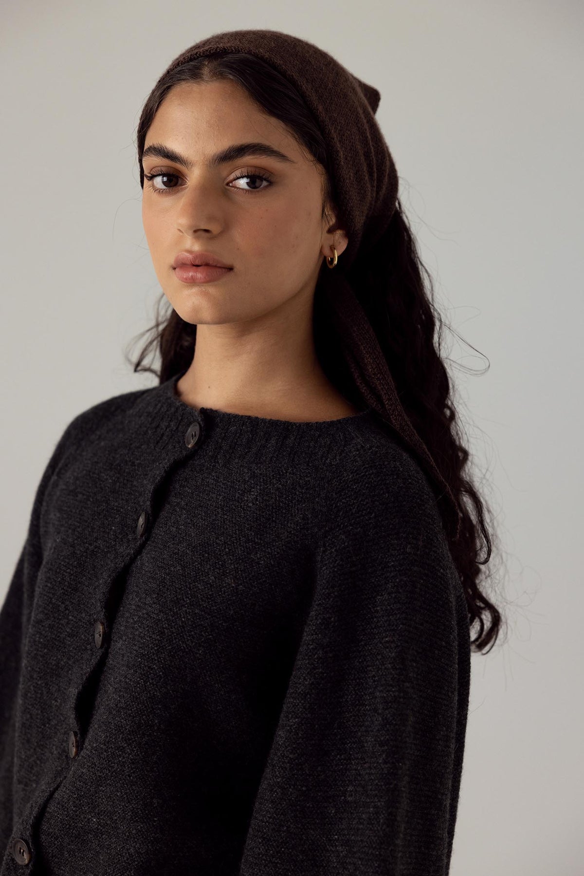 The model is wearing a black Merino Wool sweater and a black Francie Daisy Scarf – Cocoa headband.