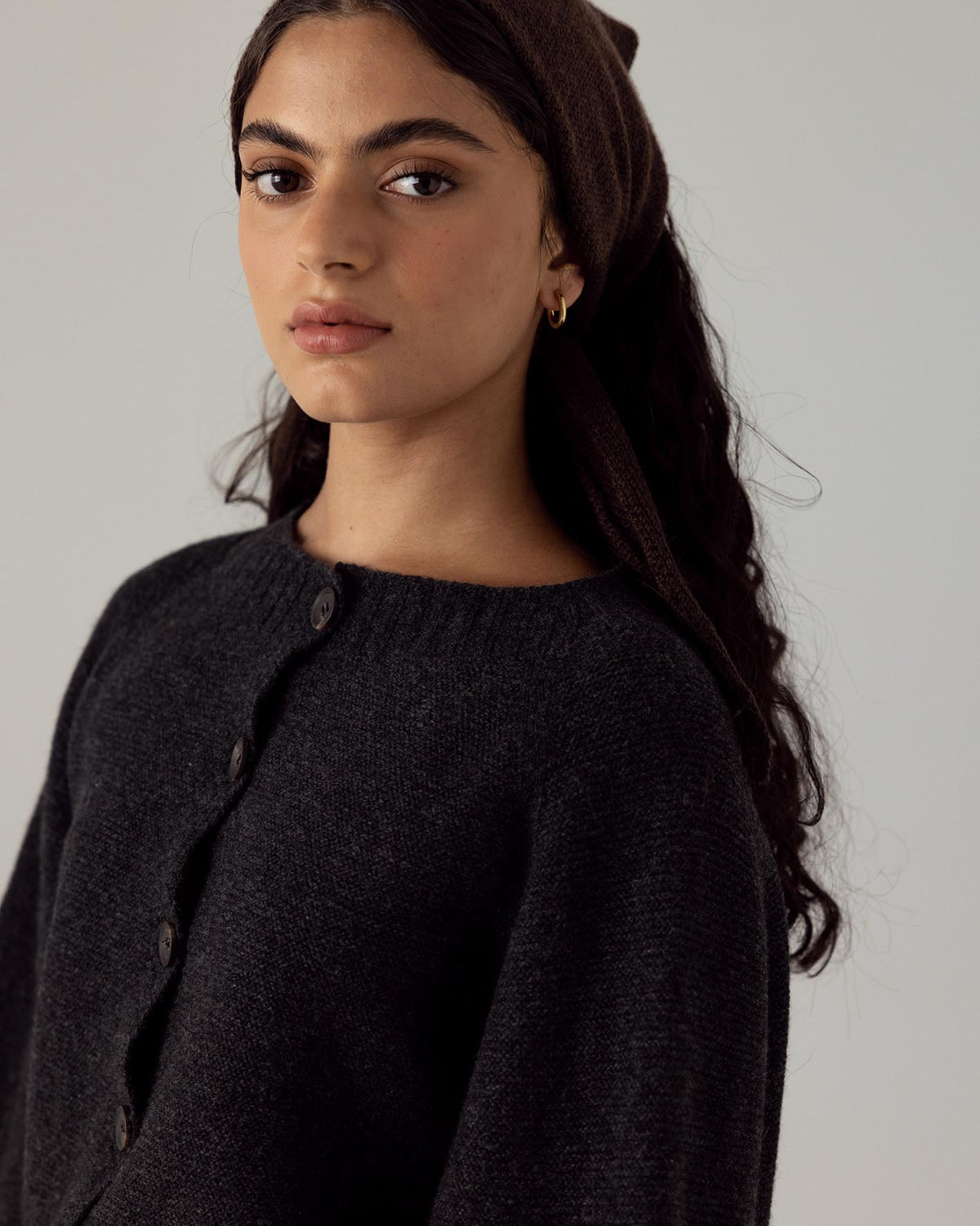 The model is wearing a black Merino Wool sweater and a black Francie Daisy Scarf – Cocoa headband.