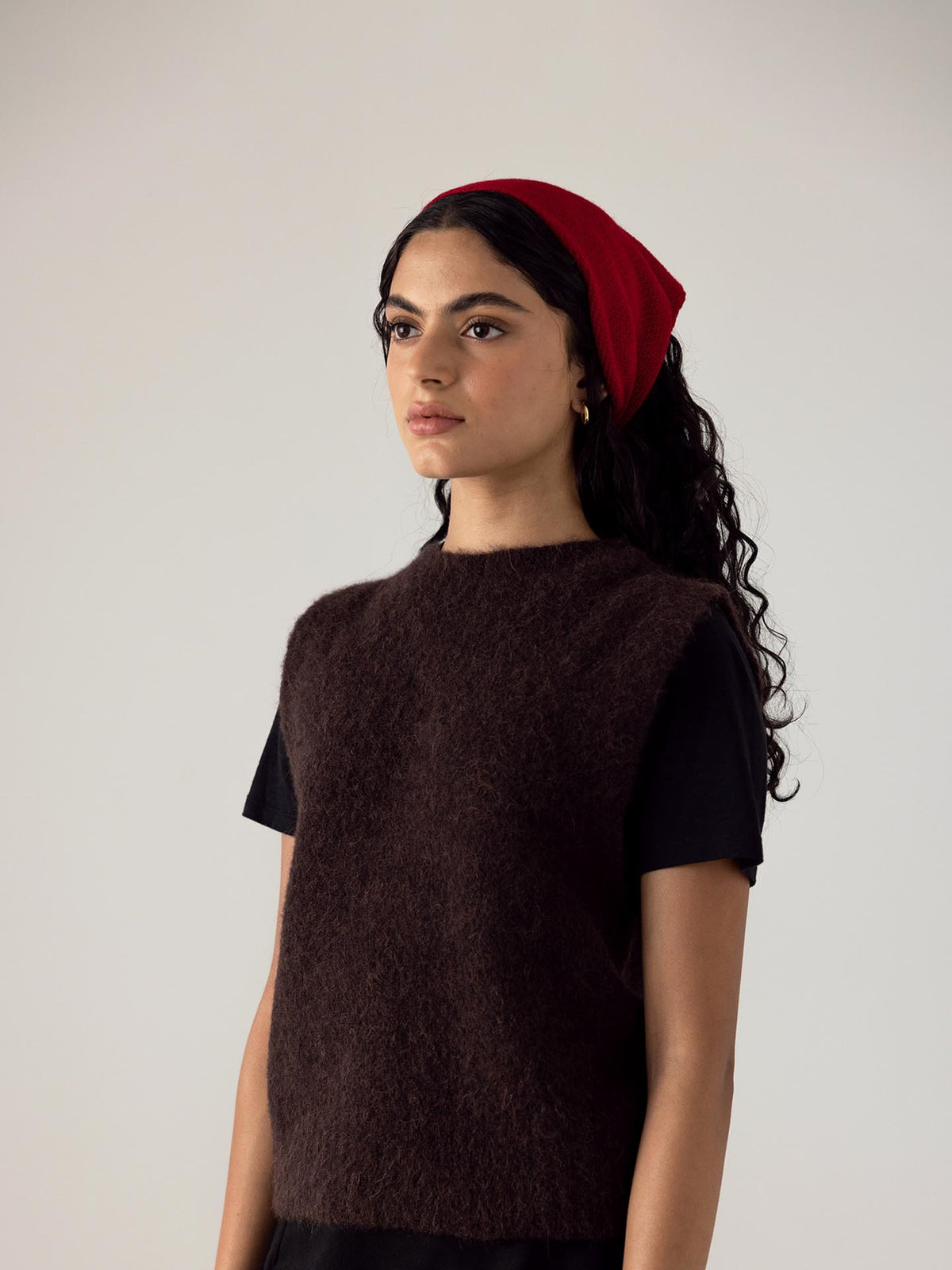 The model is wearing an ethically made brown Merino Wool sweater and a Francie red Daisy Scarf – Crimson.