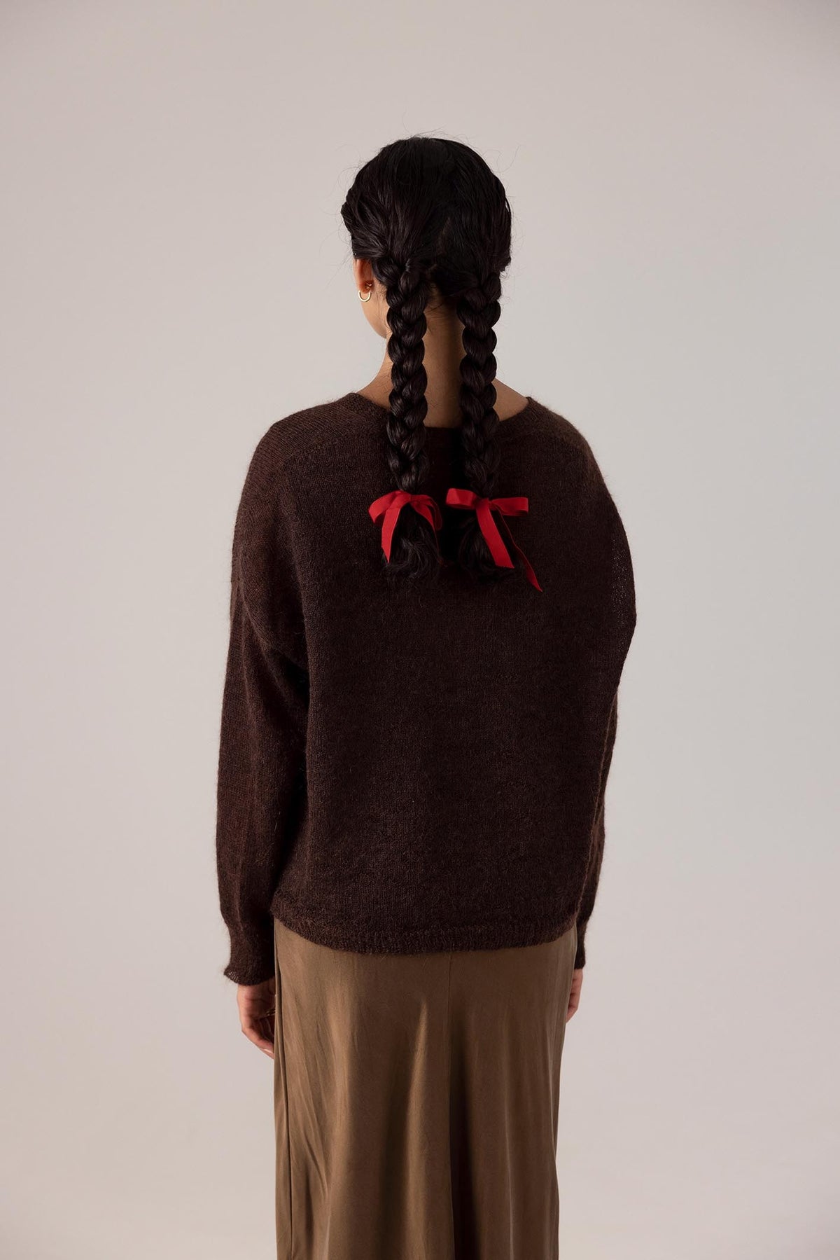 The back view of a woman wearing a Francie Feather Knit – Cocoa sweater with a red bow.