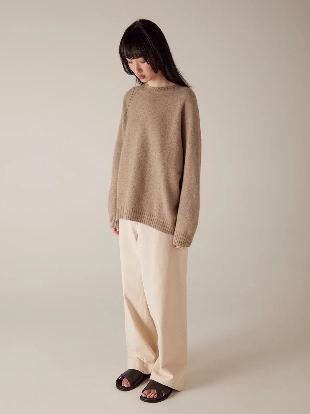 Woman wearing a Francie Nimbus Raglan Knit – Natural sweater and cream pants, standing pensively against a neutral background.