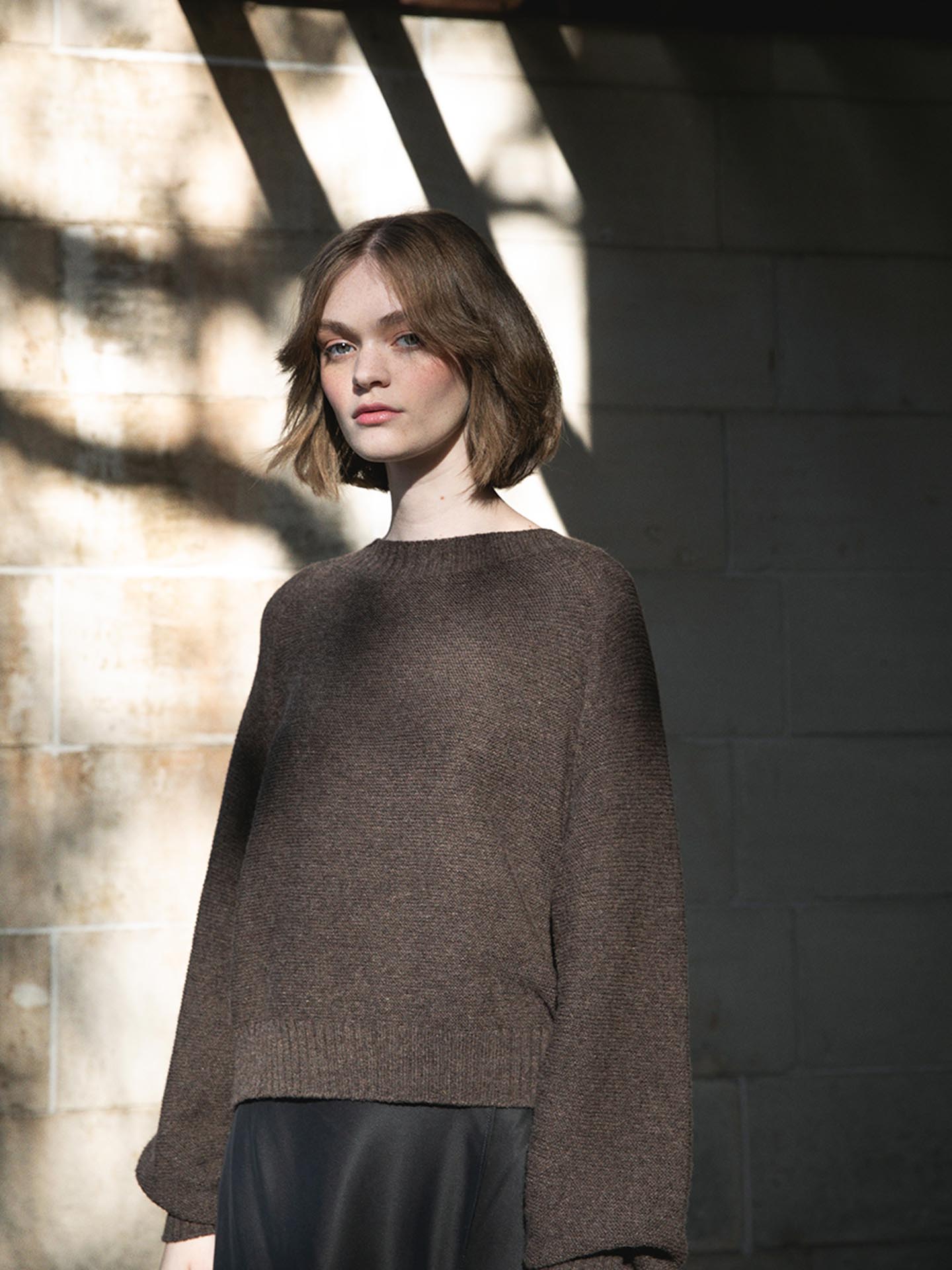 A woman wearing an oversized Francie Poet Knit - Truffle sweater and black skirt.