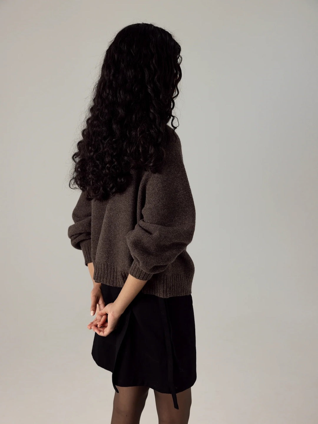 A woman with long hair wearing a Francie Poet Knit – Truffle and black skirt.