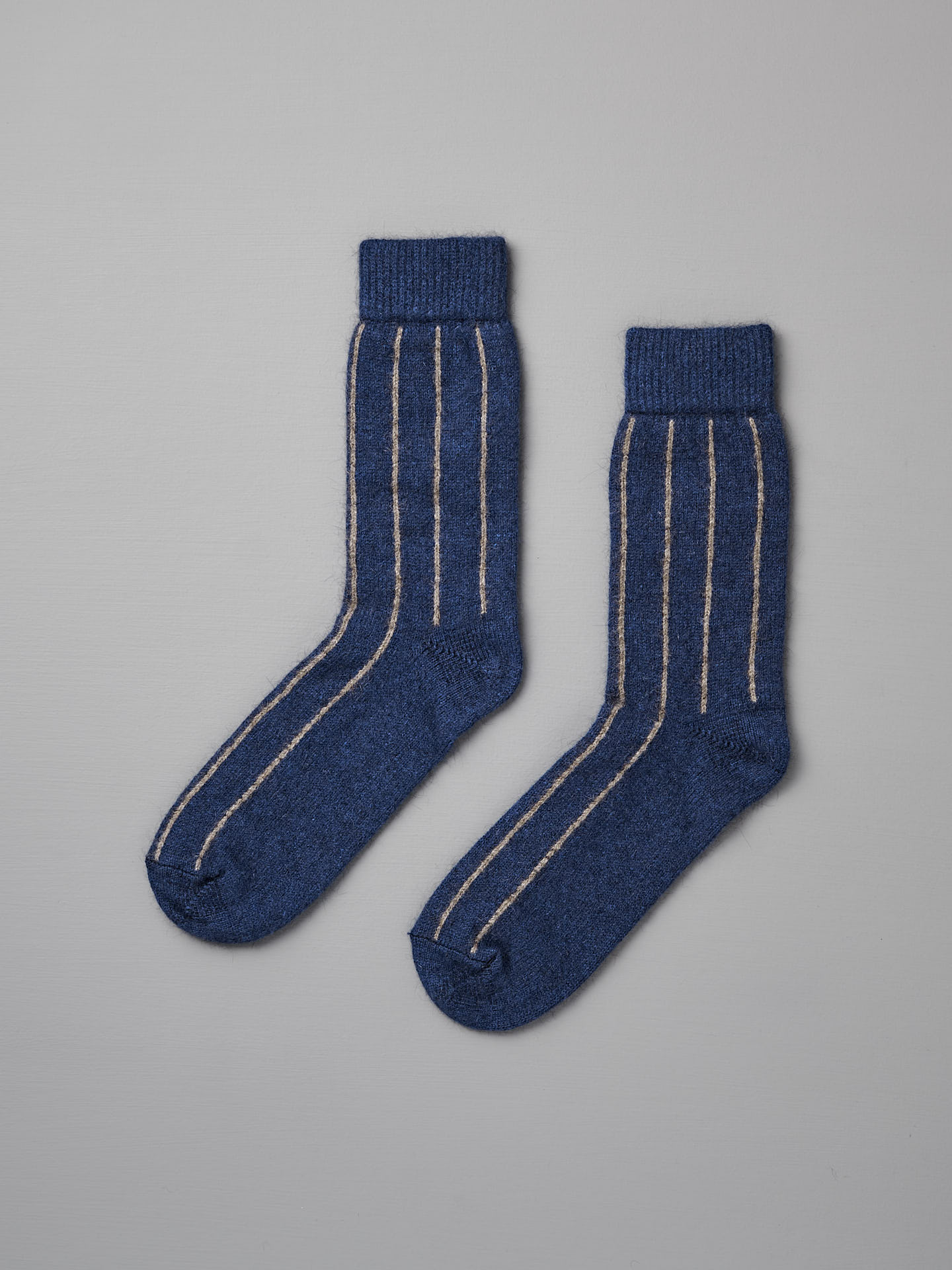 A pair of Francie Possum Merino Socks – Blue & Natural Stripe lying flat on a light gray surface.