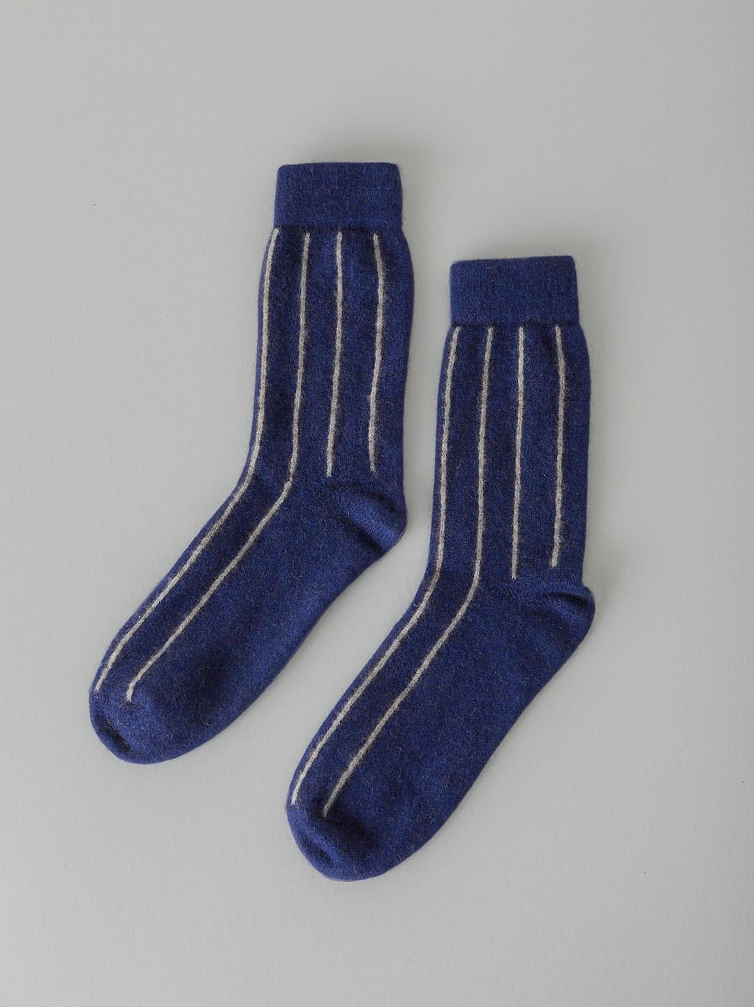 A pair of Francie Possum Merino Socks – Blue & Natural Stripe lying flat on a light gray surface.