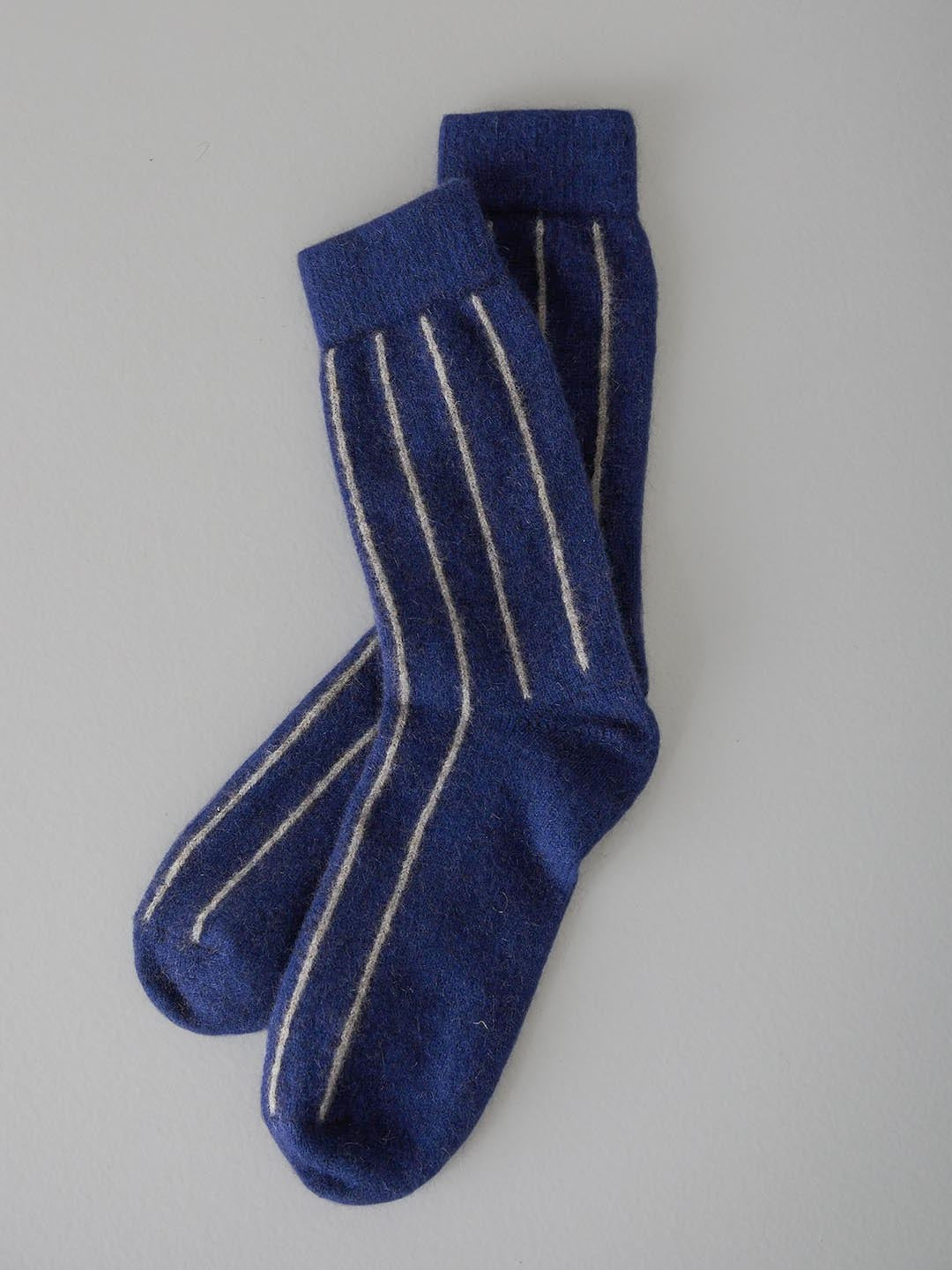 A pair of blue Francie Possum Merino Socks with white stripes laid flat on a light background.