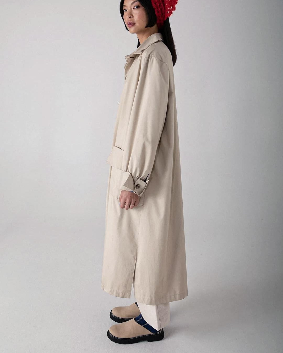 A woman stands in a neutral pose, wearing a beige trench coat, dark trousers, black strapped shoes, and Possum Merino Socks – Blue & Natural Stripe by Francie.