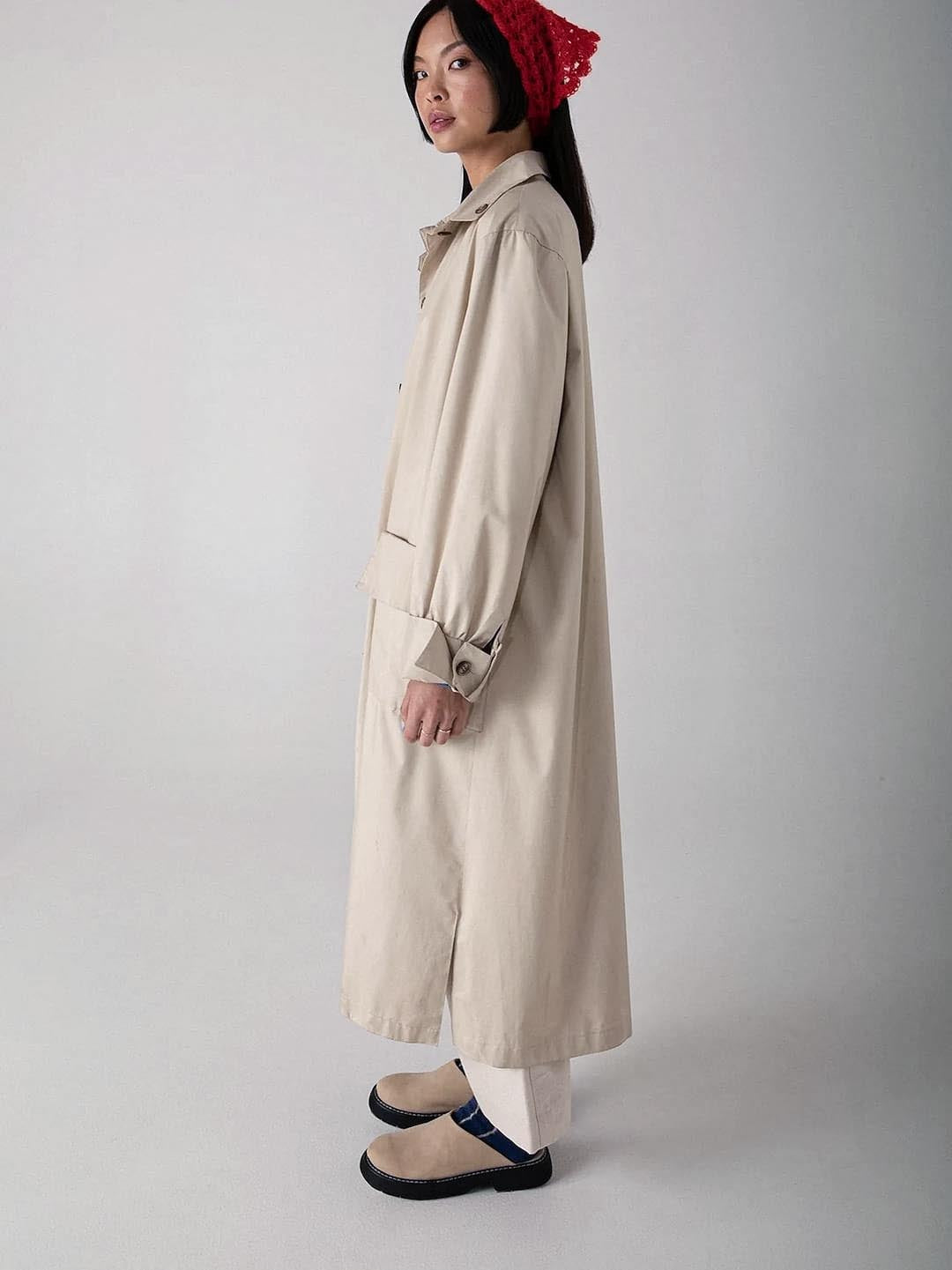 A woman stands in a neutral pose, wearing a beige trench coat, dark trousers, black strapped shoes, and Possum Merino Socks – Blue &amp; Natural Stripe by Francie.