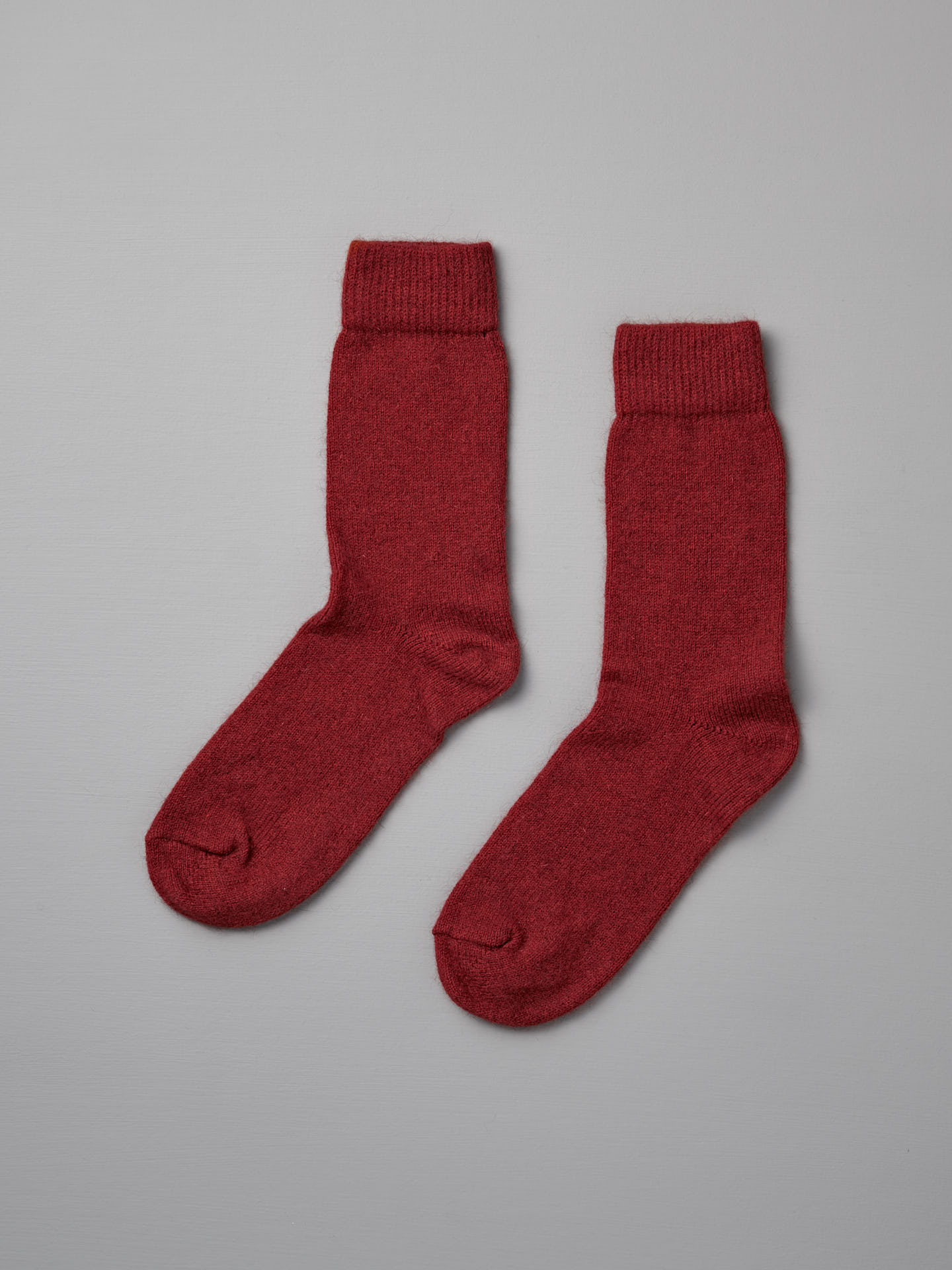 A pair of Francie Possum Merino Socks – Crimson, suitable for various shoe sizes, laid flat on a light beige background.