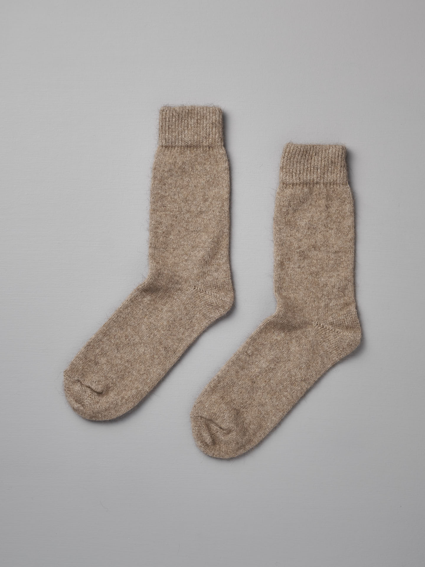 A pair of Possum Merino Socks – Natural from Francie laid flat on a gray surface.