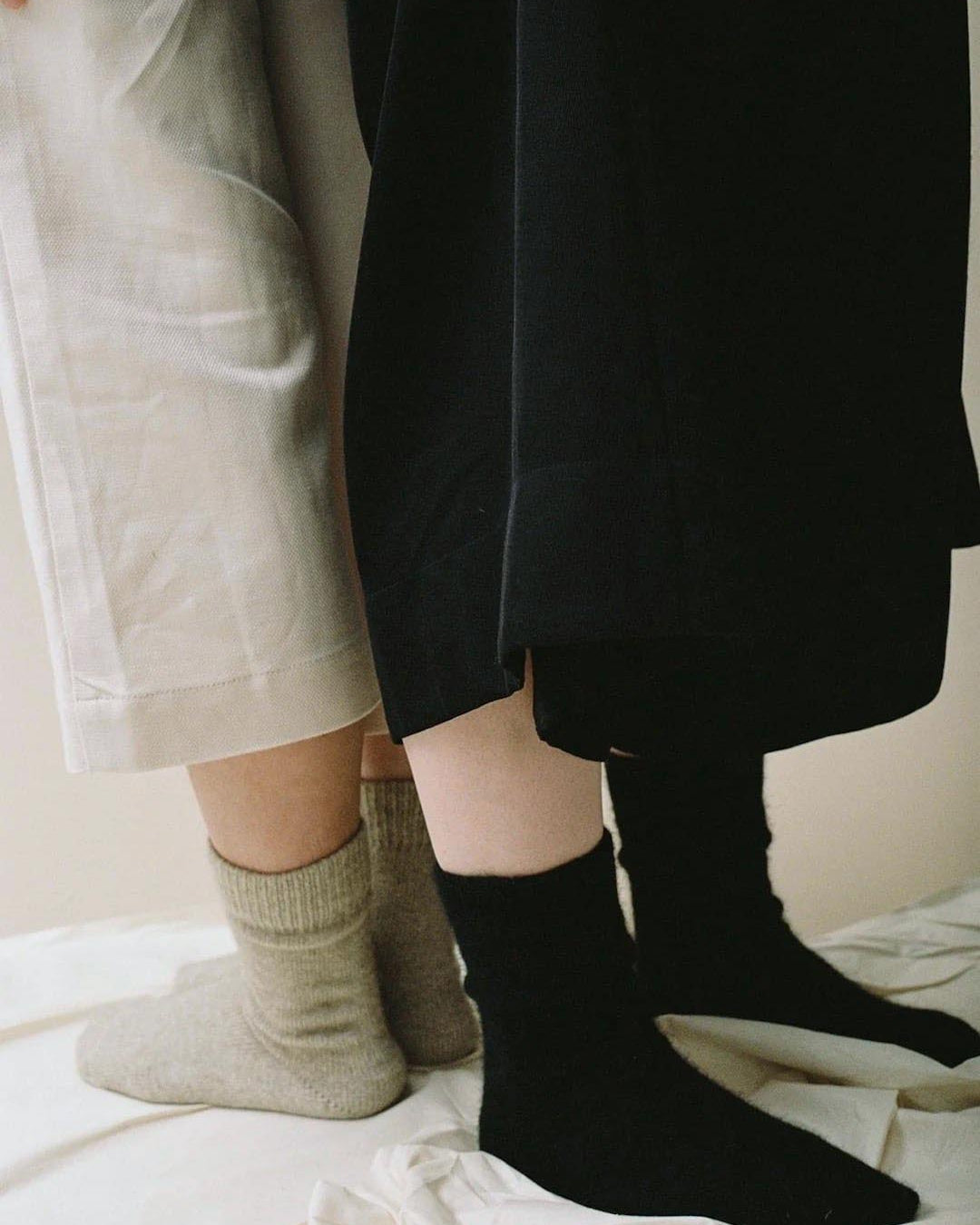 Two people standing side by side in New Zealand, with the camera focused on their lower half, wearing different colored Francie Possum Merino socks and pants.
