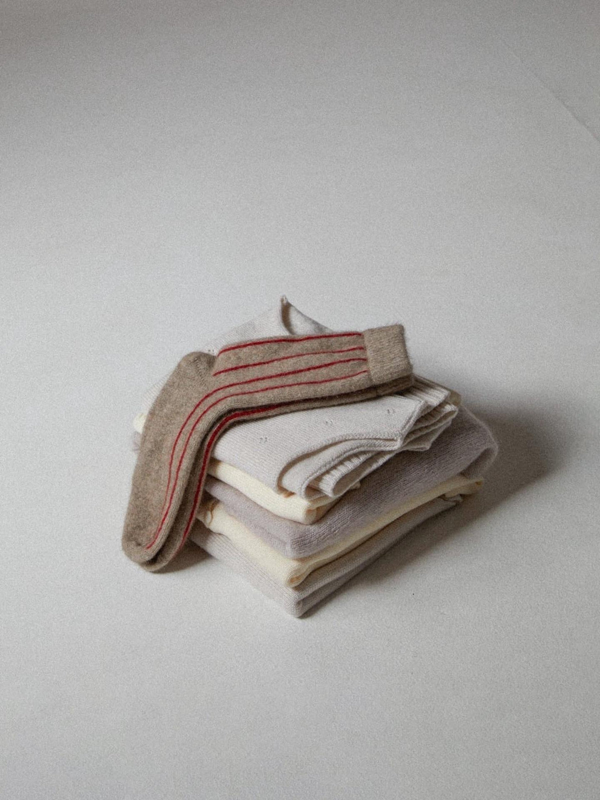 A stack of neatly folded Possum Merino Socks – Natural &amp; Poppy Stripe by Francie on a plain background.