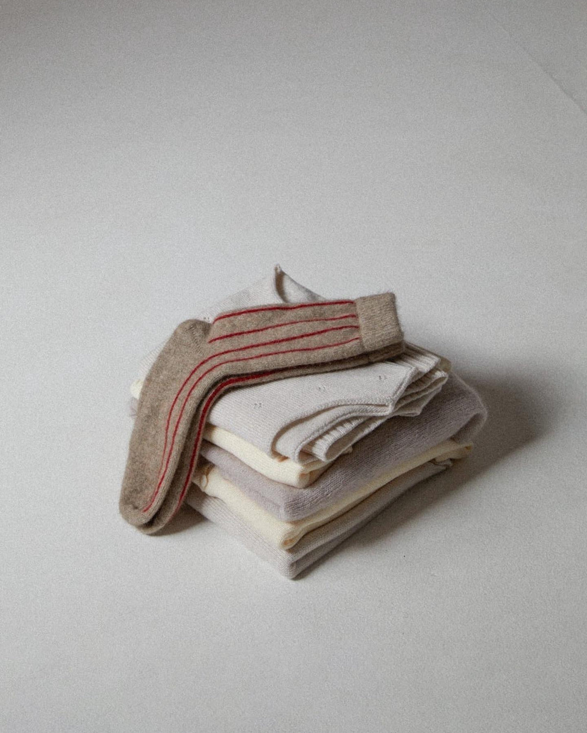 A stack of neatly folded Possum Merino Socks – Natural & Poppy Stripe by Francie on a plain background.