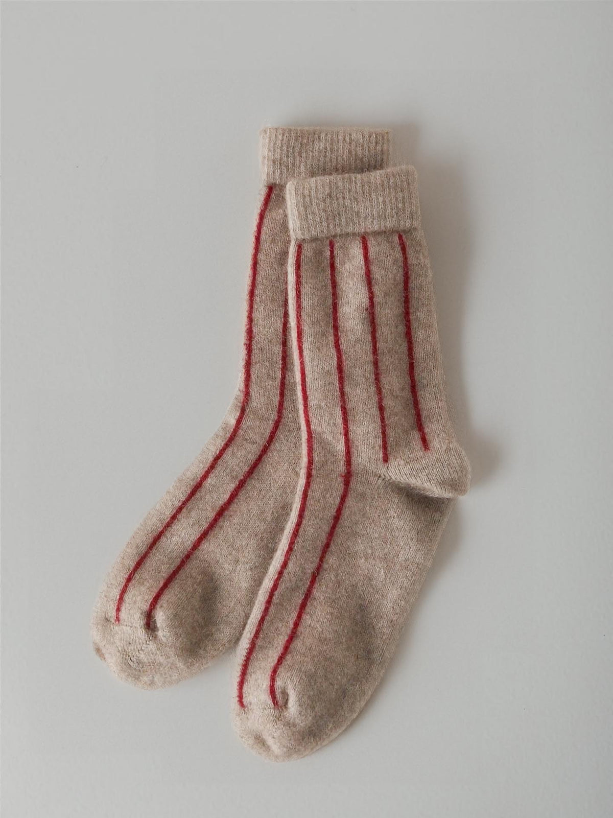 A pair of beige Possum Merino Socks by Francie with red stripes on a light gray background.
