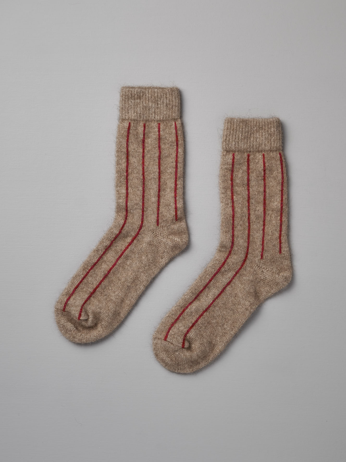 A pair of beige Possum Merino Socks by Francie with red stripes on a light gray background.