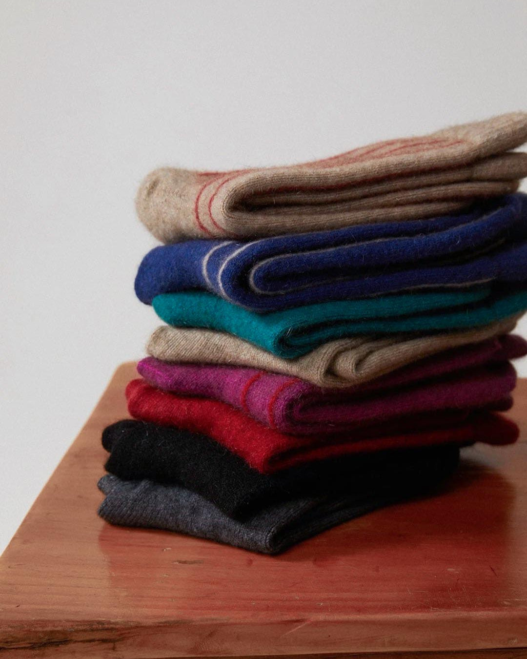 A neat stack of folded Possum Merino socks in Orchid & Poppy Stripe placed on a wooden table.