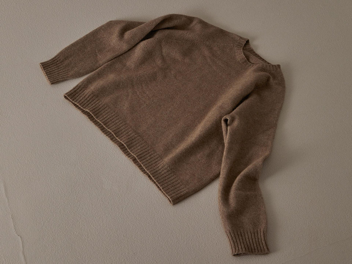 A brown, relaxed fit Nimbus Raglan Knit – Natural sweater laid flat on a textured beige surface by Francie.