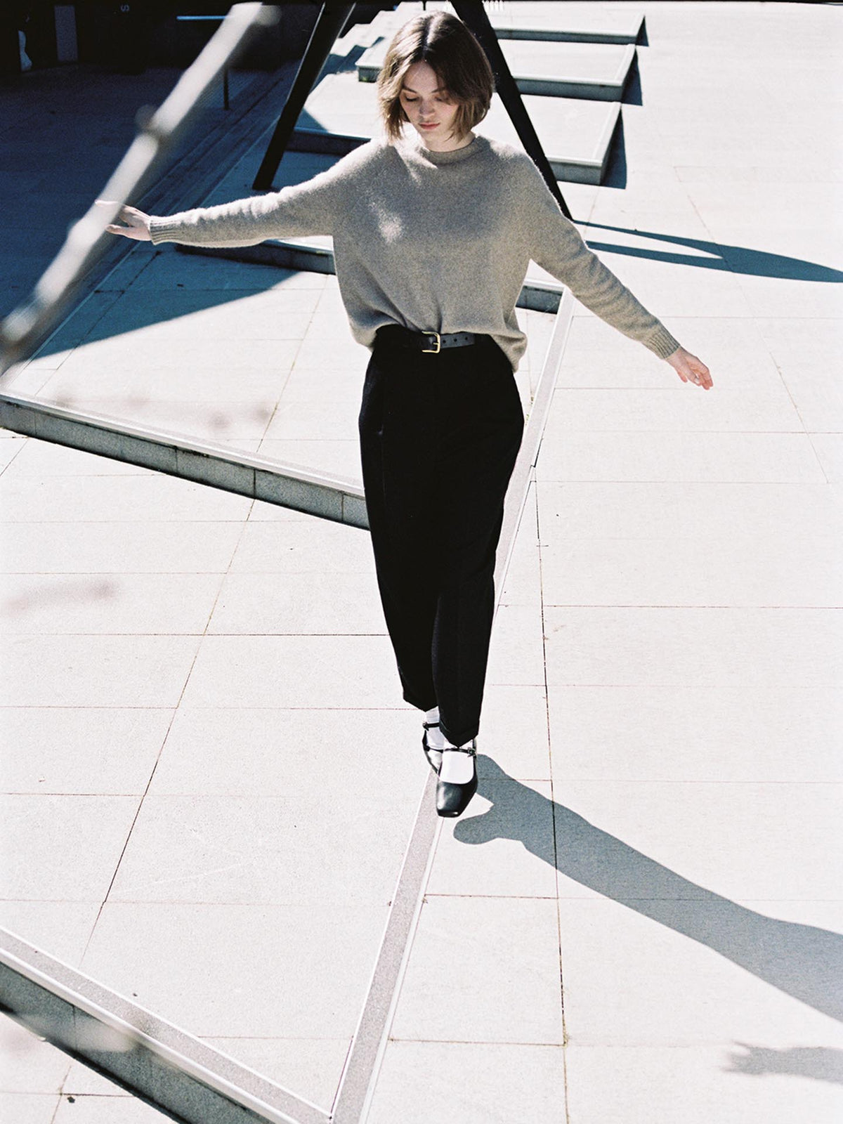 A young woman in a relaxed fit, casual outfit descends an outdoor staircase, sunlight casting shadows on the steps wearing the Francie Nimbus Raglan Knit - Natural.