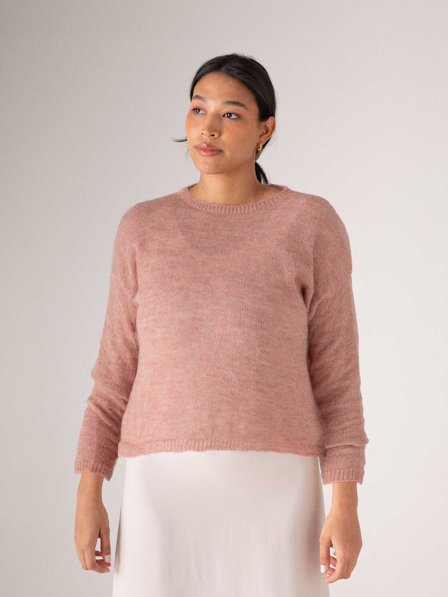 A person in a cozy, oversized Francie Feather Knit sweater in dusk pink, paired with a white skirt, stands against a plain background.