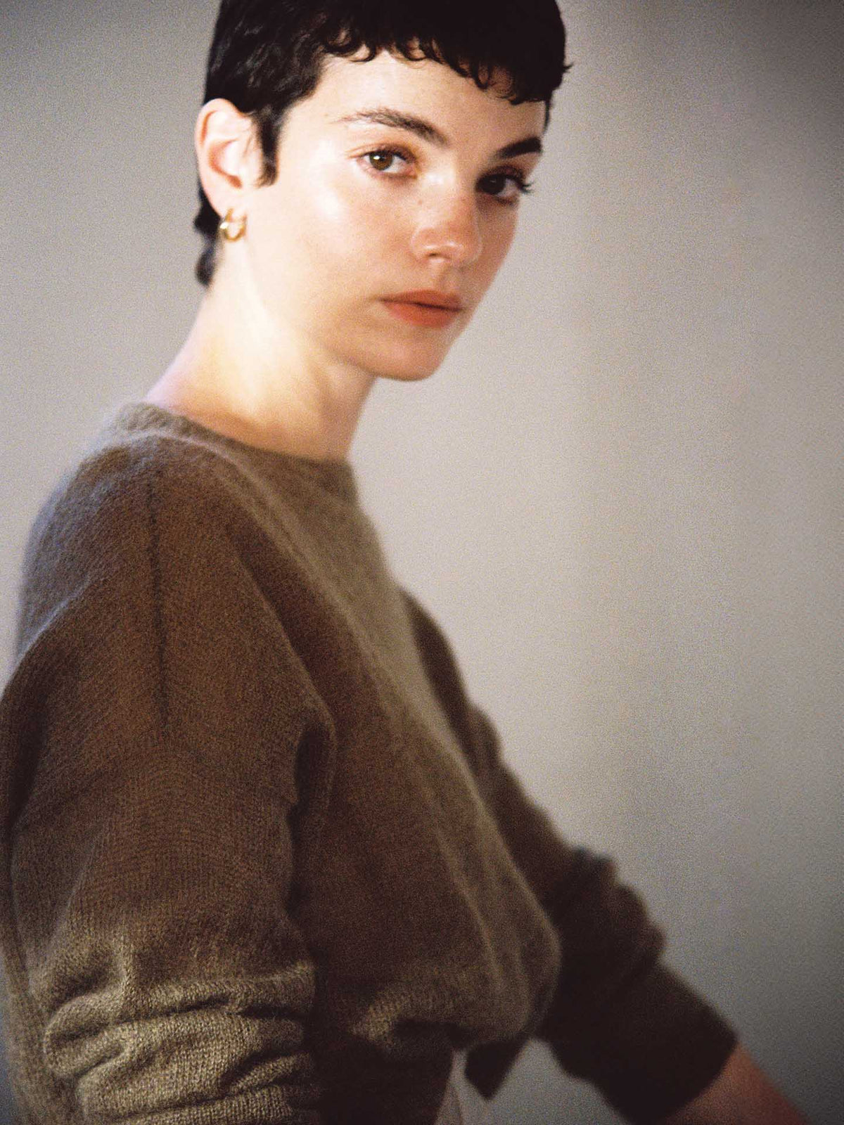 A person with short dark hair is wearing the Francie Feather Knit Hazel sweater, looking towards the camera against a plain background.