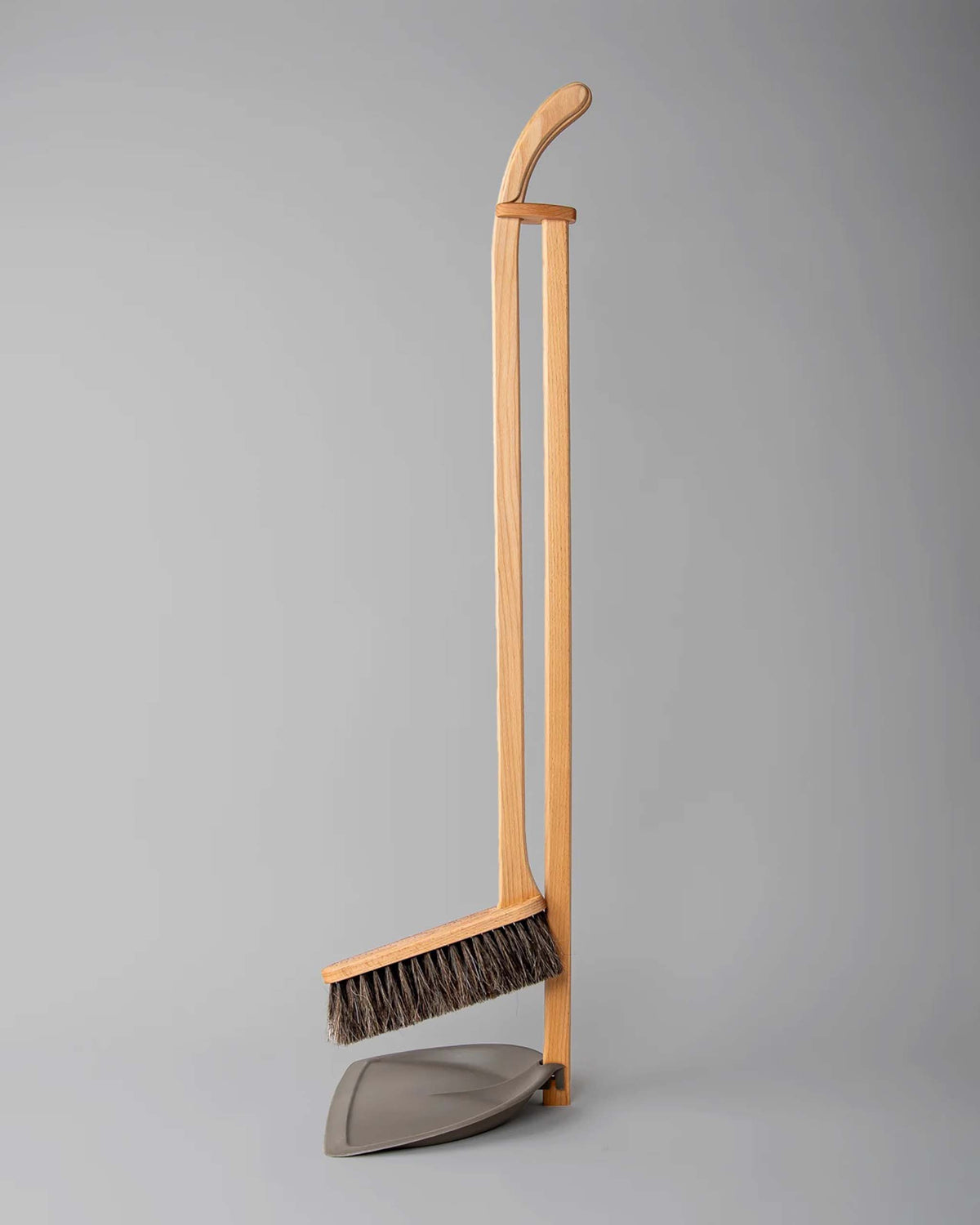 A wooden broom with dark bristles and a matching dustpan are propped upright together against a plain gray background.