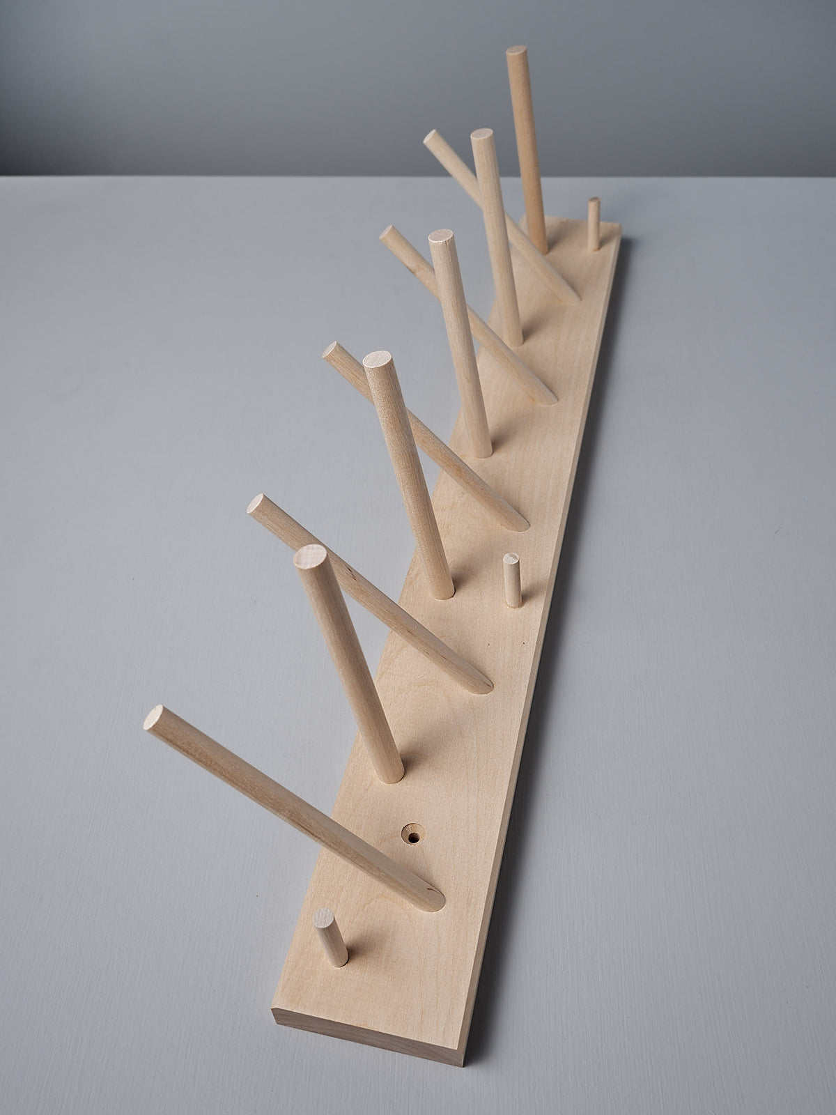 The Multihanger Rack – Birch by Iris Hantverk boasts a wooden peg rack made from untreated birch, complete with a rectangular base and multiple dowels positioned at different angles for elegant organization.