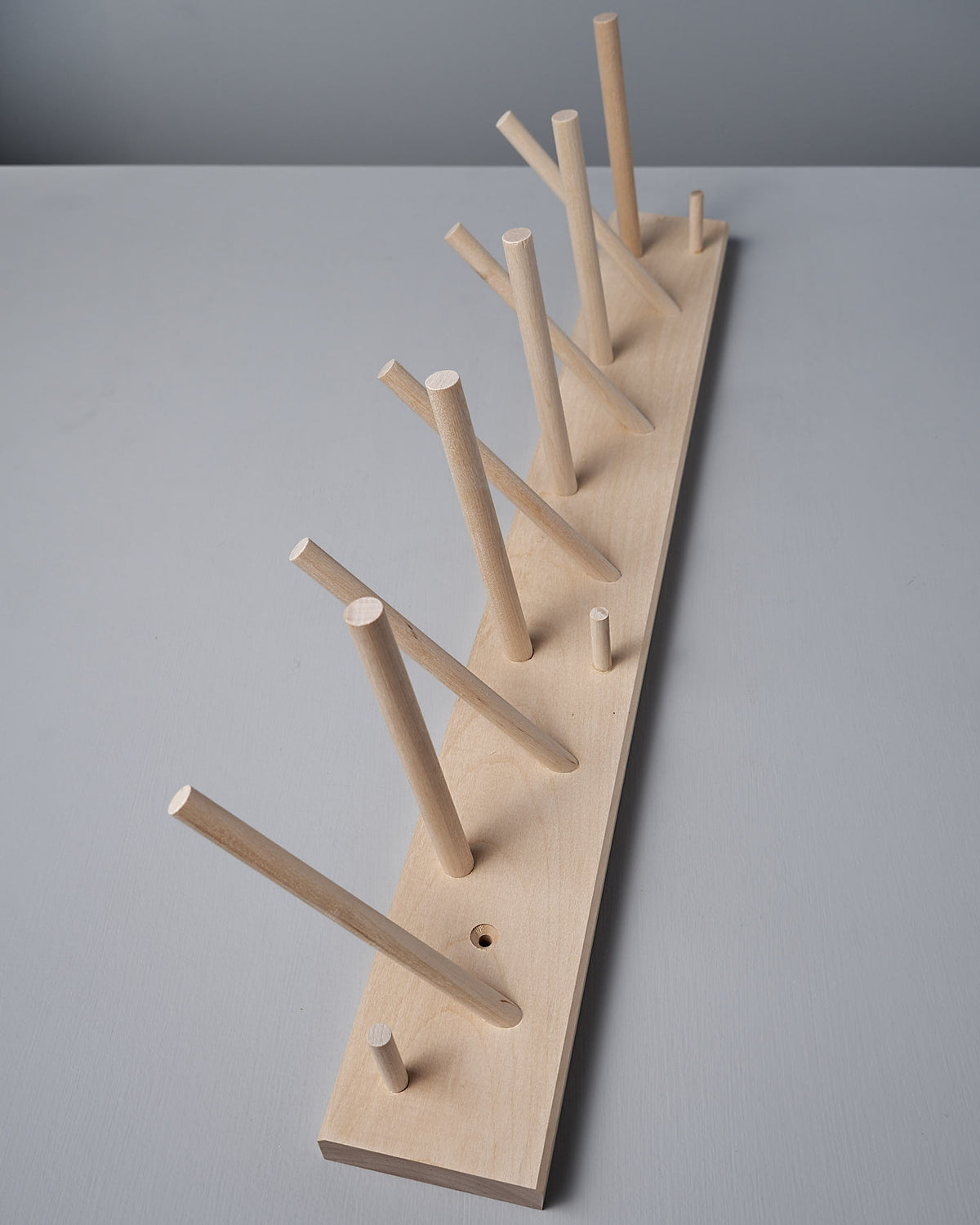 The Multihanger Rack – Birch by Iris Hantverk boasts a wooden peg rack made from untreated birch, complete with a rectangular base and multiple dowels positioned at different angles for elegant organization.