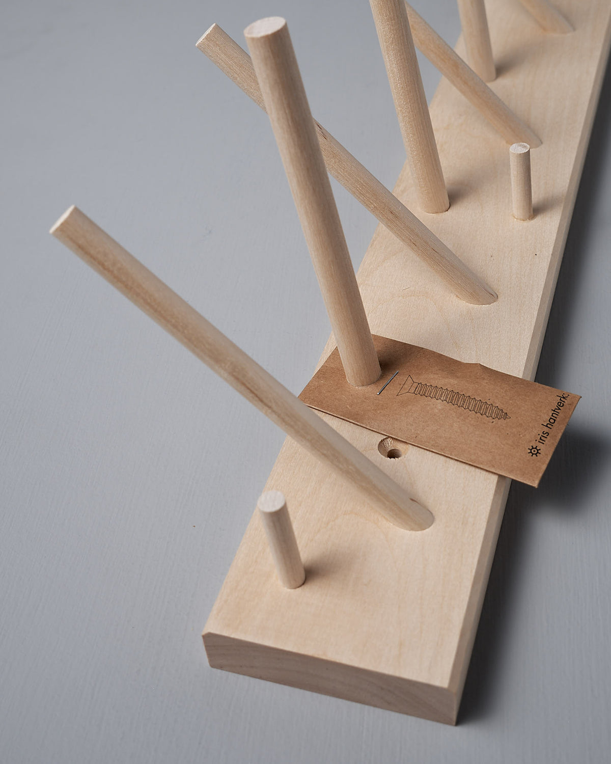 The Multihanger Rack – Birch by Iris Hantverk is crafted from untreated birch, featuring dowels protruding at various angles and a brown tag with a screw illustration resting on it, effortlessly combining functionality and artisan design.