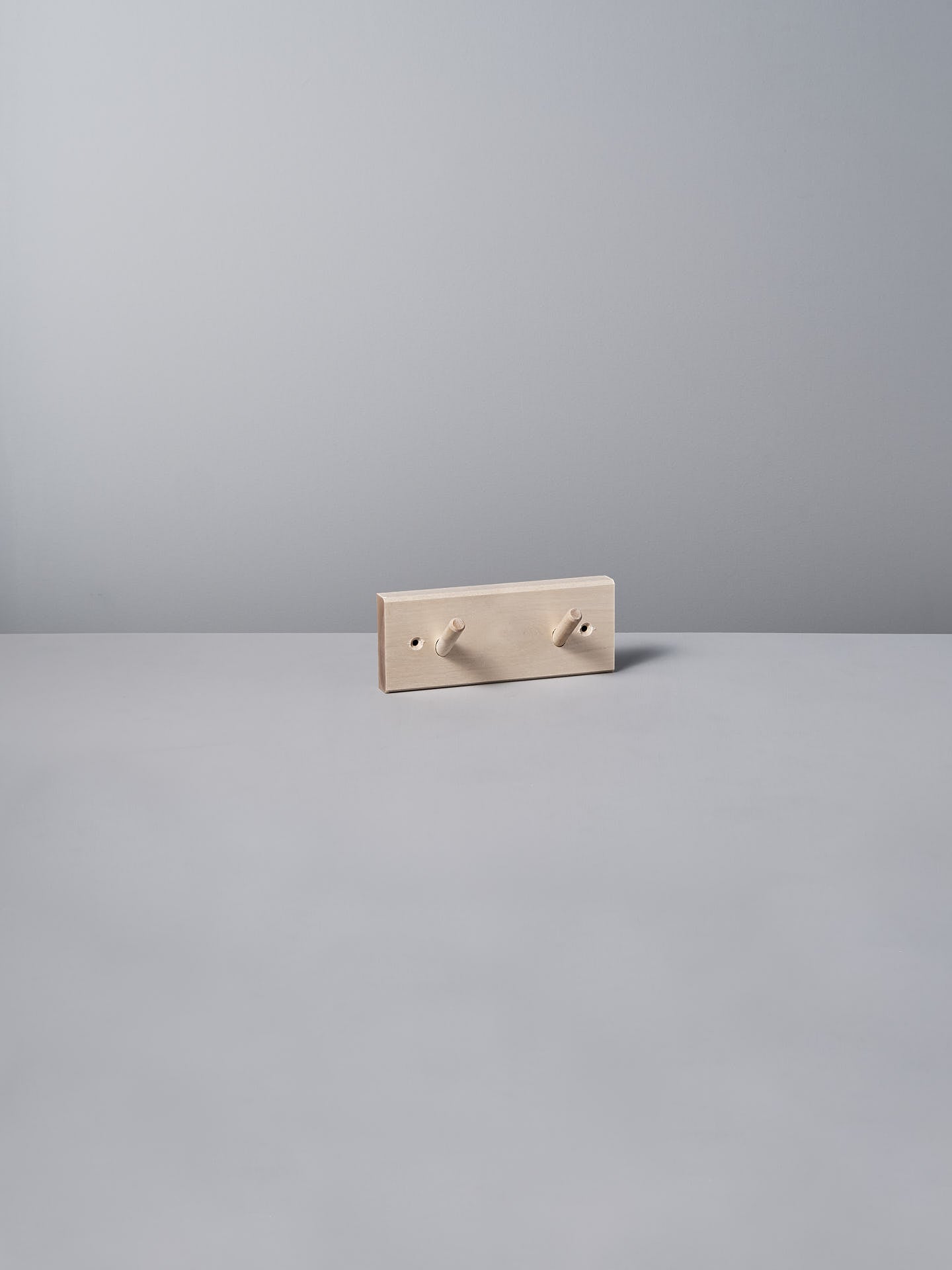 The Birchwood Peg Rail – 2 Hook by Iris Hantverk, with its minimalist beige design inspired by Shaker craftsmanship, elegantly stands against a light gray background, highlighting the timeless charm of untreated birch.