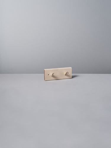The Birchwood Peg Rail – 2 Hook by Iris Hantverk, with its minimalist beige design inspired by Shaker craftsmanship, elegantly stands against a light gray background, highlighting the timeless charm of untreated birch.