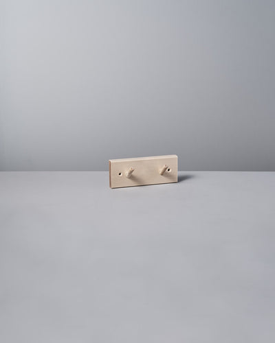 The Birchwood Peg Rail – 2 Hook by Iris Hantverk, with its minimalist beige design inspired by Shaker craftsmanship, elegantly stands against a light gray background, highlighting the timeless charm of untreated birch.