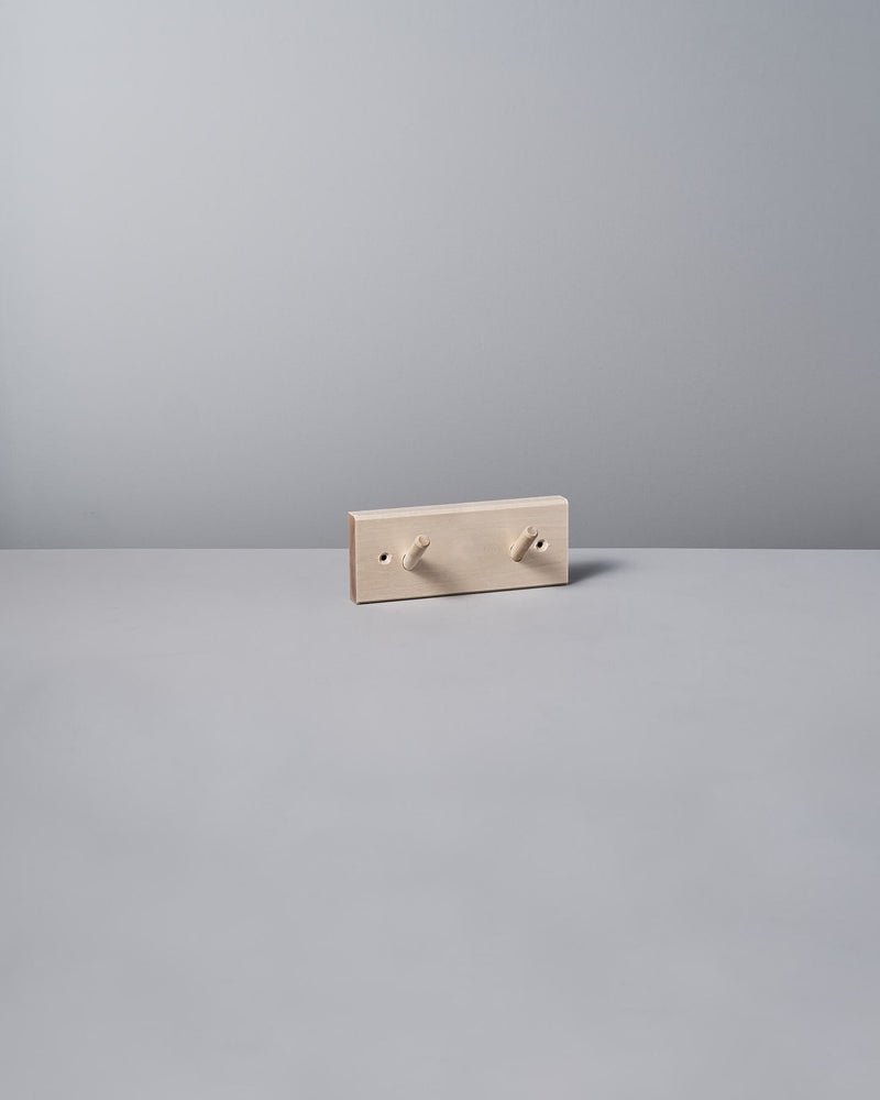 The Birchwood Peg Rail – 2 Hook by Iris Hantverk, with its minimalist beige design inspired by Shaker craftsmanship, elegantly stands against a light gray background, highlighting the timeless charm of untreated birch.