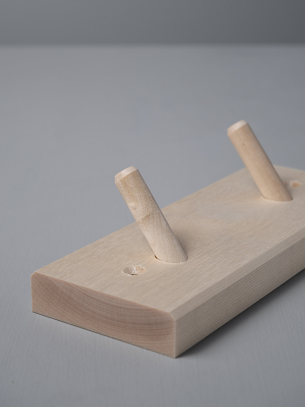 The Birchwood Peg Rail – 2 Hook, crafted by Iris Hantverk, features an untreated Birch wooden block with two angled pegs inspired by Shaker design, elegantly set against a subtle gray background.