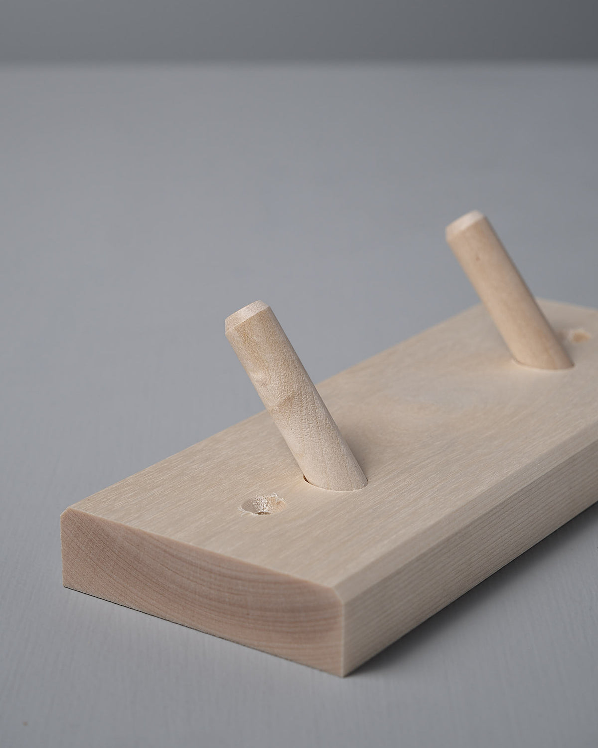 The Birchwood Peg Rail – 2 Hook, crafted by Iris Hantverk, features an untreated Birch wooden block with two angled pegs inspired by Shaker design, elegantly set against a subtle gray background.
