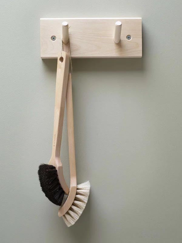 An Iris Hantverk Birchwood Peg Rail featuring two hooks, crafted from untreated birch, elegantly displays a wooden dish brush with bristles on both ends.