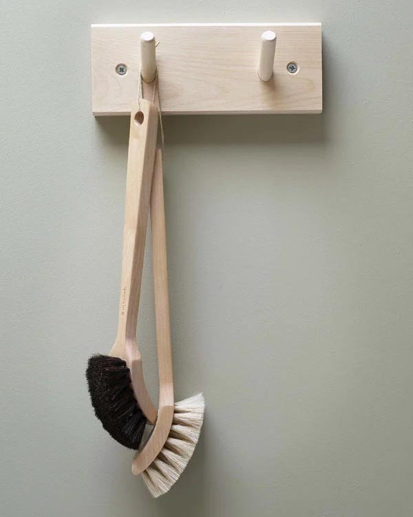 An Iris Hantverk Birchwood Peg Rail featuring two hooks, crafted from untreated birch, elegantly displays a wooden dish brush with bristles on both ends.