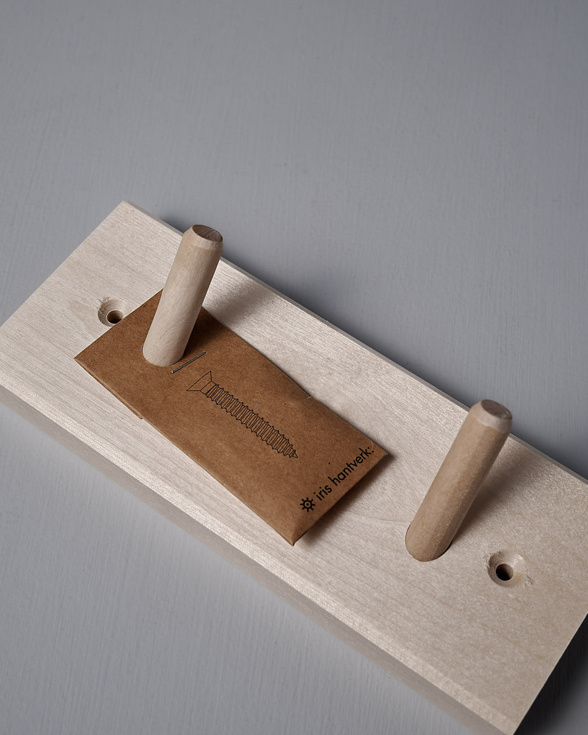 The Birchwood Peg Rail – 2 Hook by Iris Hantverk is ideal for home organization, featuring two shaker-inspired hooks and comes with a small brown envelope and a screw illustration.