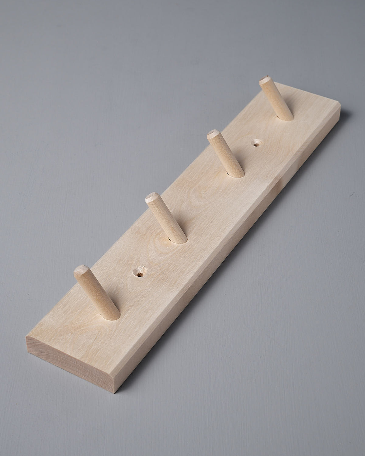 The Birchwood Peg Rail – 4 Hook by Iris Hantverk, crafted from untreated birch, rests gracefully on a light gray surface, showcasing the brand's timeless design.