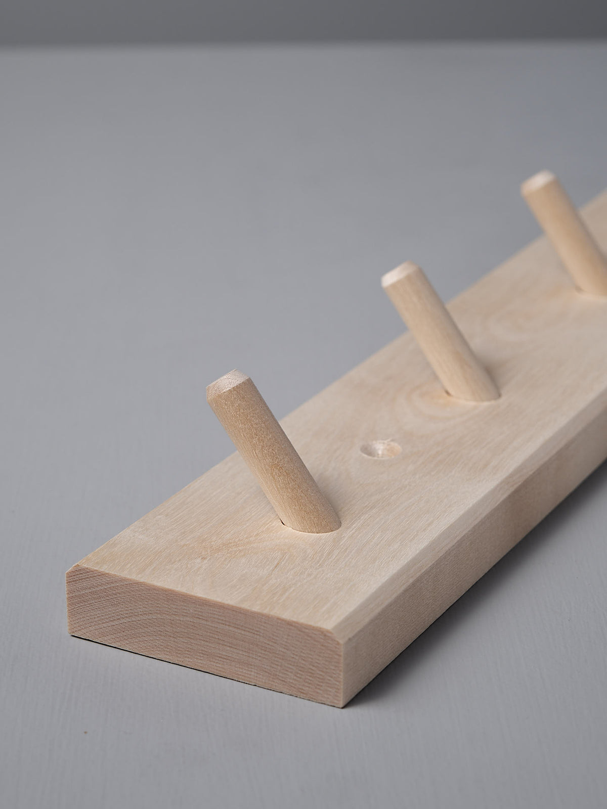 The Birchwood Peg Rail – 4 Hook by Iris Hantverk, crafted from untreated birch, features four angled pegs for hanging items. Its Shaker-inspired design seamlessly combines simplicity with functionality.