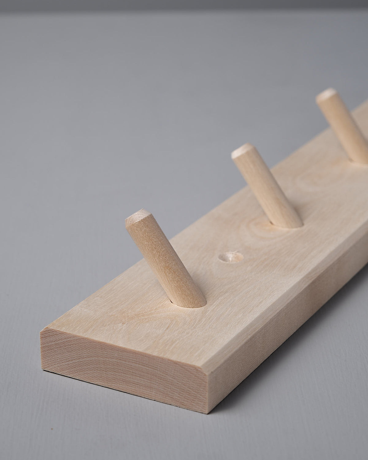 The Birchwood Peg Rail – 4 Hook by Iris Hantverk, crafted from untreated birch, features four angled pegs for hanging items. Its Shaker-inspired design seamlessly combines simplicity with functionality.