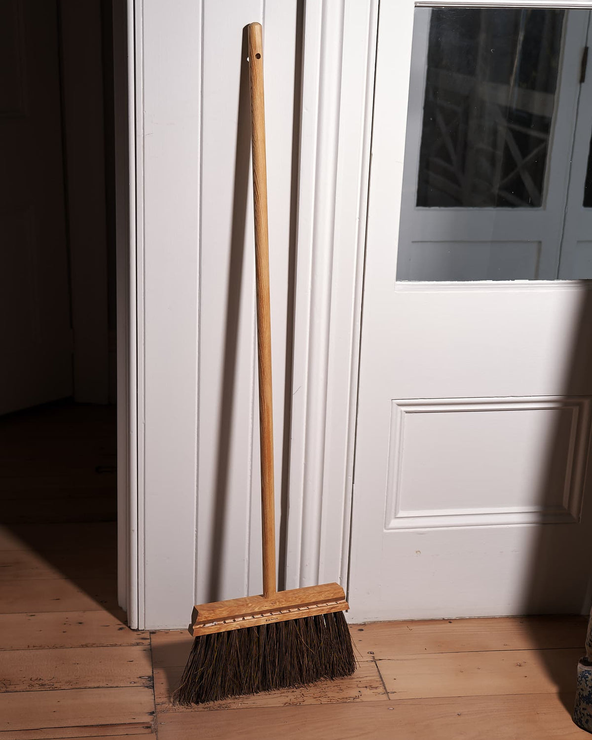 An Outdoor Broom - Birch & Bassine by Iris Hantverk leaning against a door.