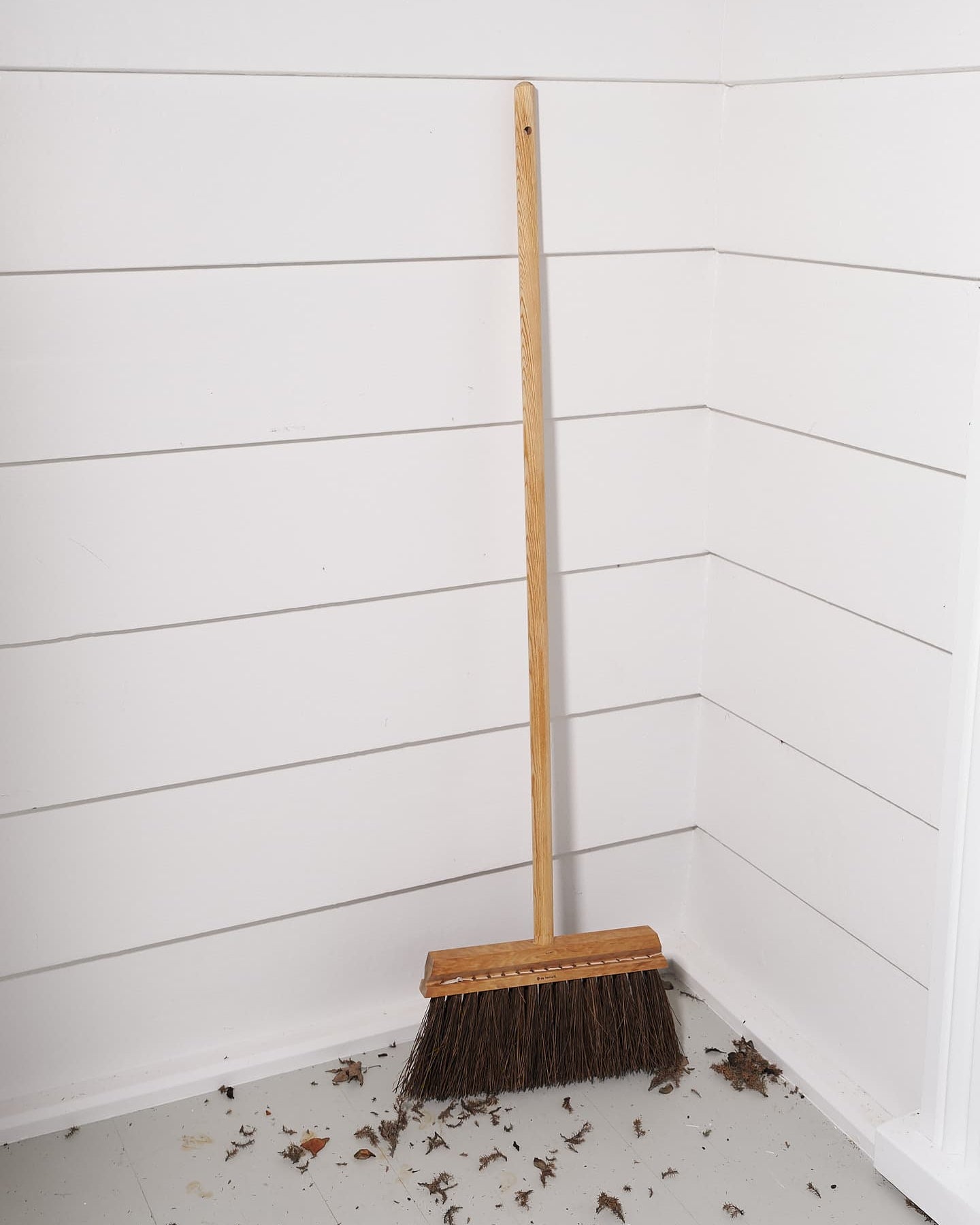 An Outdoor Broom – Birch & Bassine, made by Iris Hantverk, sitting on the floor of a room.