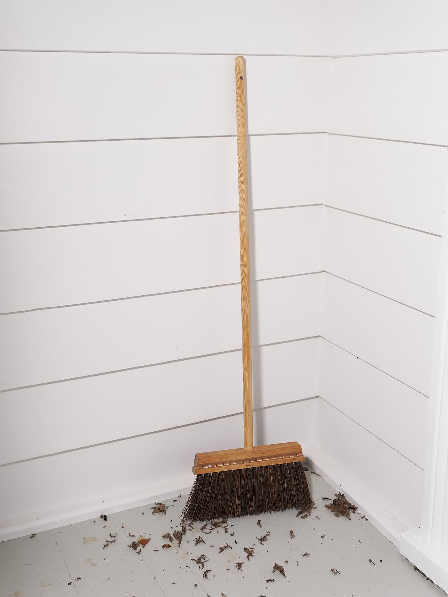 An Outdoor Broom – Birch & Bassine, made by Iris Hantverk, sitting on the floor of a room.
