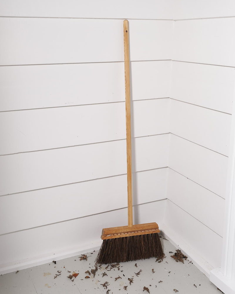 An Outdoor Broom – Birch & Bassine, made by Iris Hantverk, sitting on the floor of a room.